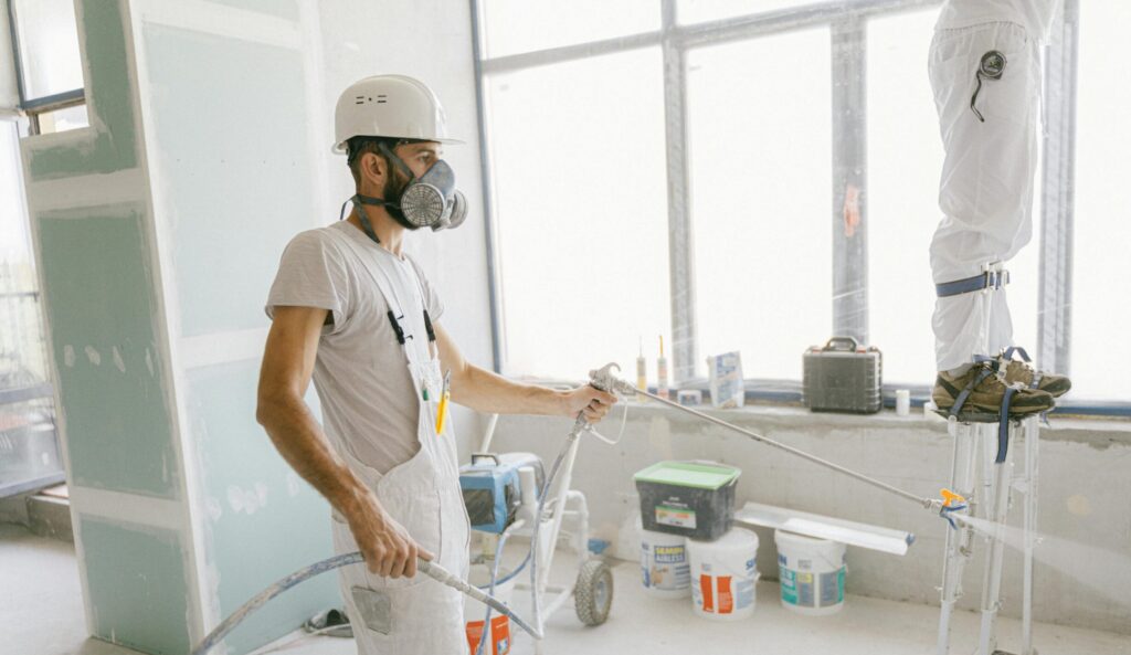 Two construction workers wearing protective gear and painting interior walls for a renovation project.