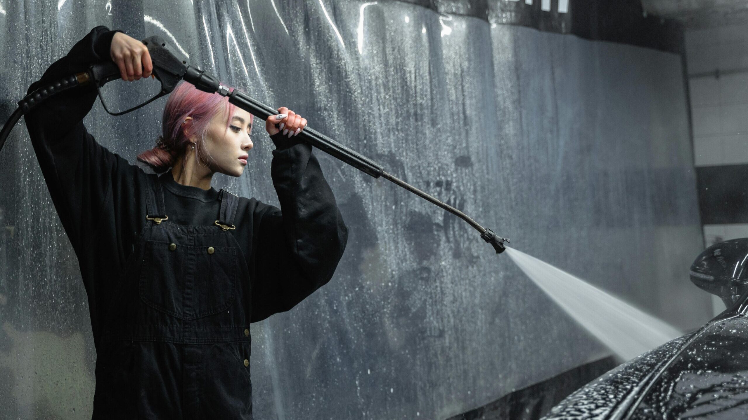 A woman using a pressure hose for car cleaning in an indoor garage.