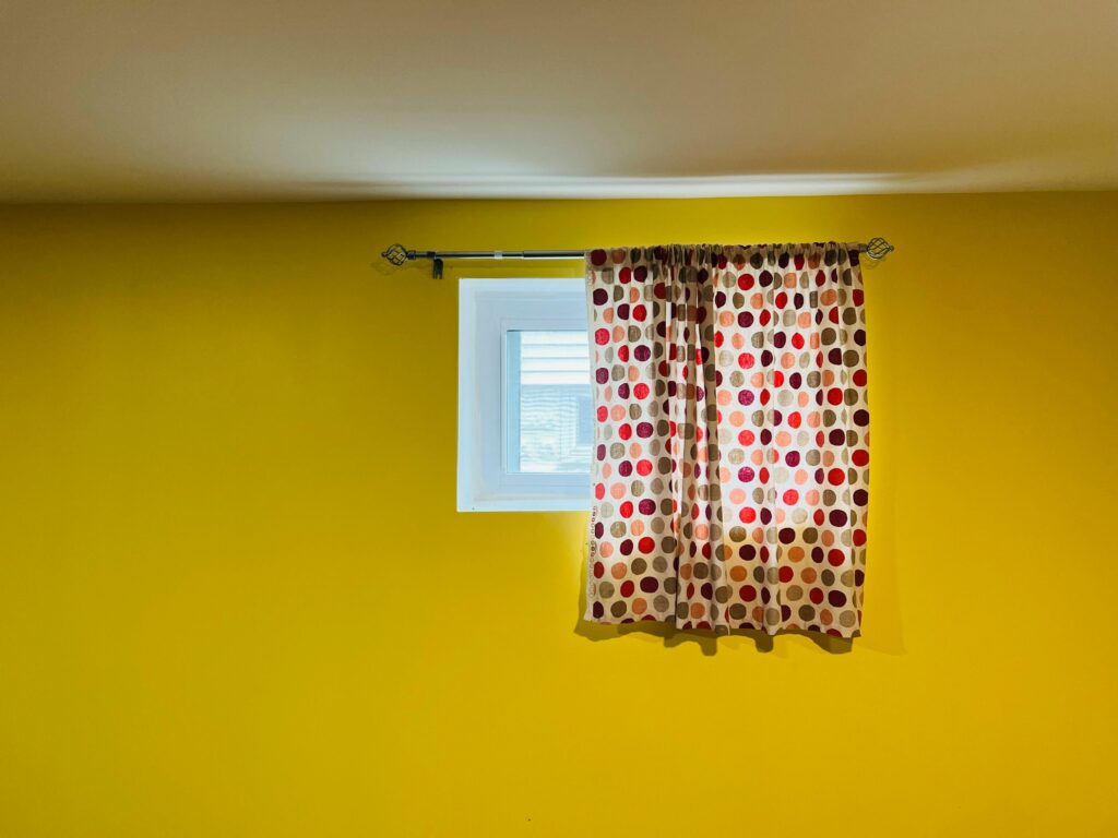 A vivid yellow wall featuring a window adorned with red and black polka dot curtains.