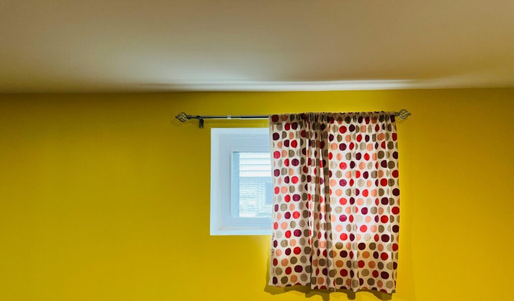 A vivid yellow wall featuring a window adorned with red and black polka dot curtains.
